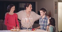 Kids and their mother singing near Hanukkah candles.