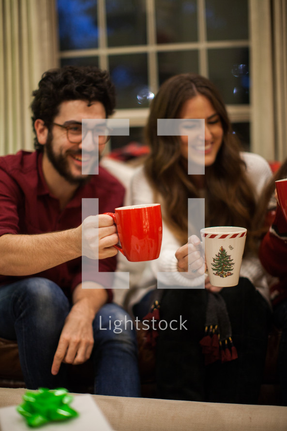 people sitting on a couch drinking hot cocoa and talking at a Christmas party 