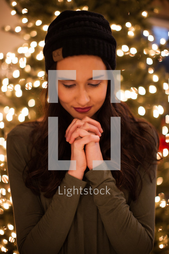 a woman praying in front of a Christmas tree 