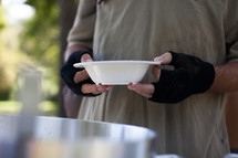A man wearing fingerless gloves holding a bowl of soup.