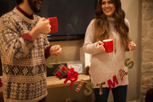 a couple holding mugs of hot cocoa and a Christmas sign 