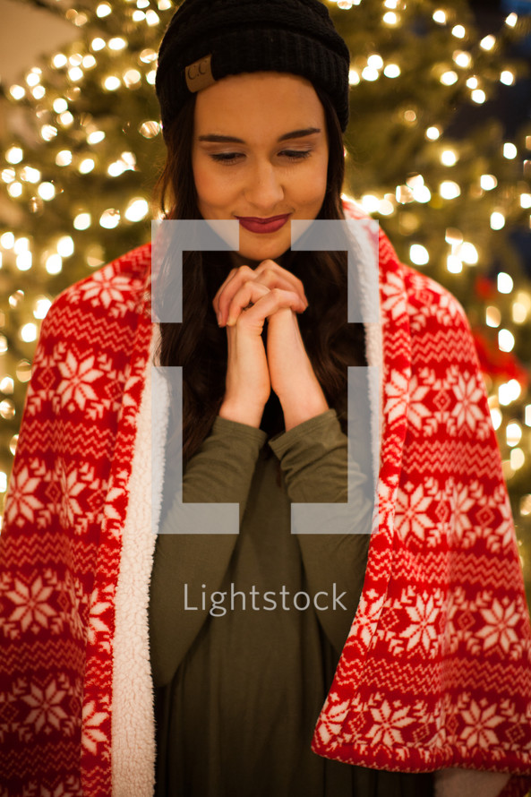 a woman standing in front of a Christmas tree with praying hands 