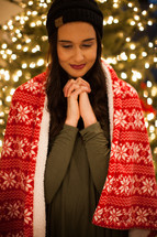 a woman standing in front of a Christmas tree with praying hands 
