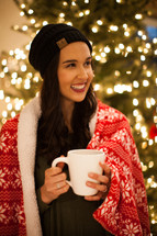 a woman with a mug of hot cocoa standing in front of a Christmas tree 
