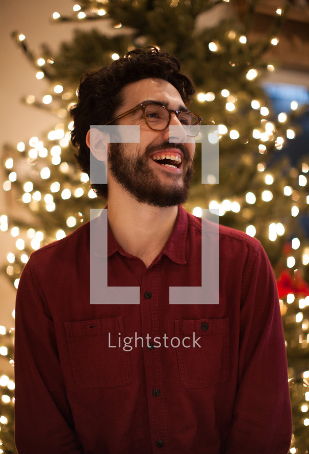 a smiling man standing in front of a Christmas tree 