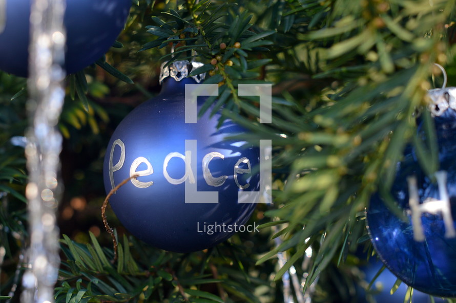 The words Peace, Grace and Hope written in silver letters on blue Christmas ornament bulbs. 
