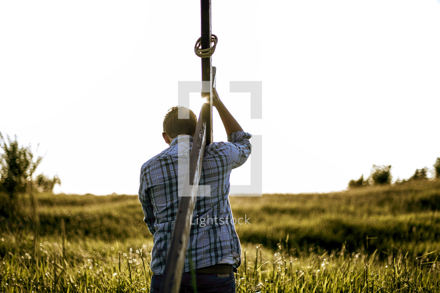 man carrying a cross through a field 