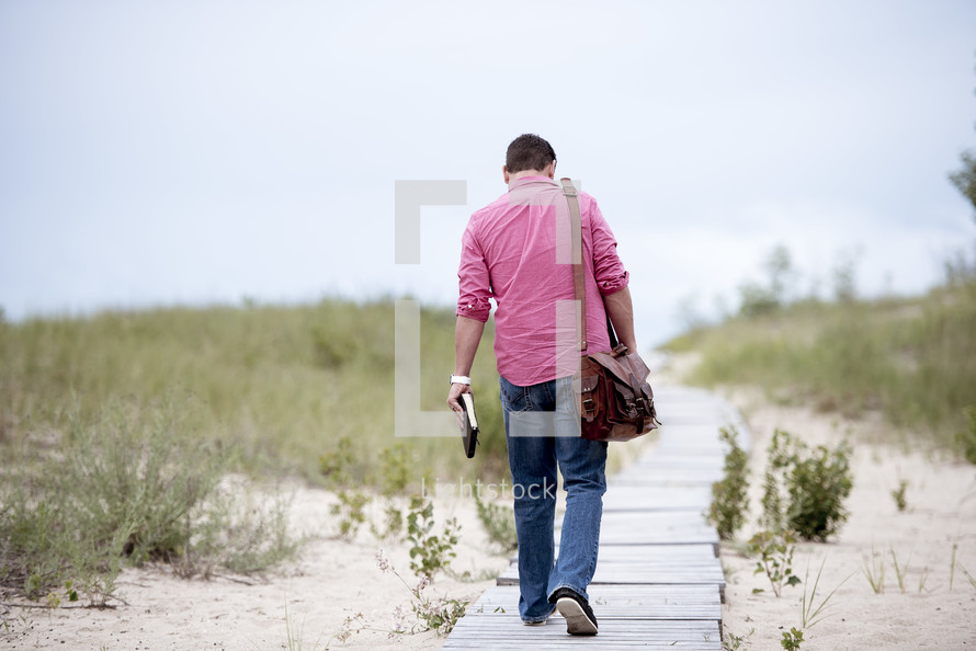 man walking on a boardwalk carrying a Bible 
