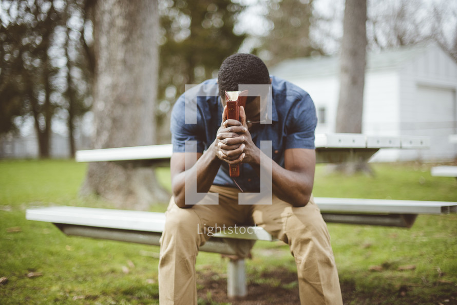 a man with head bowed holding a Bible praying 