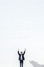 a man standing in front of a white wall with raised hands 