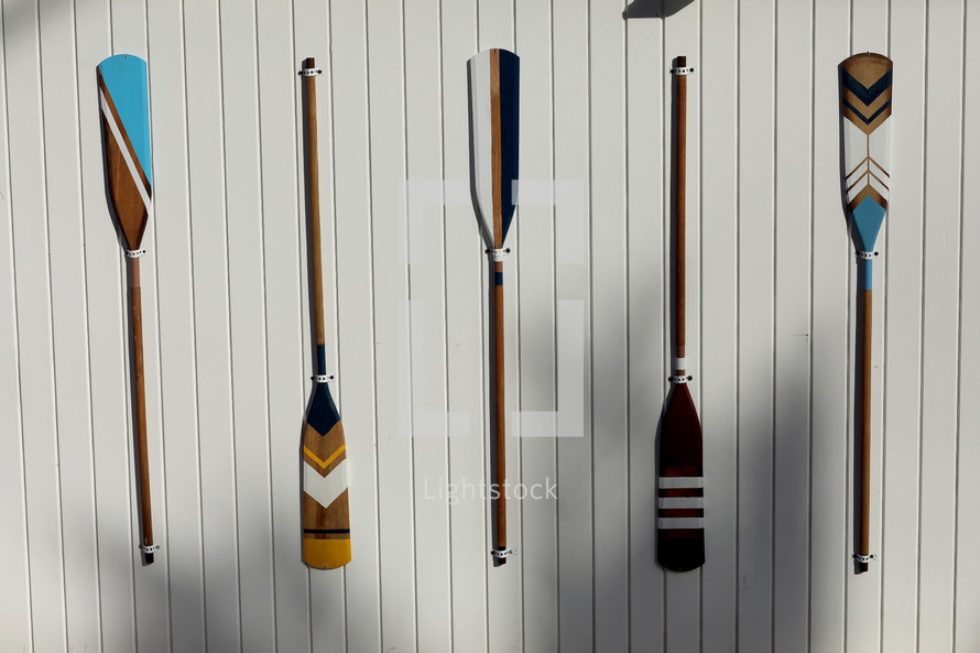 four colourful wooden paddles hangs on a white wall. canoe oars for active water sport. holiday vacation. High quality photo.