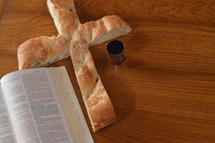 Bread in the shape of a cross with a bible open at Luke 22 and a goblet of wine. 
