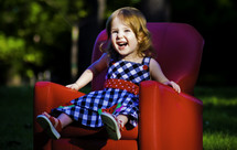 child sitting in a red chair outdoors 