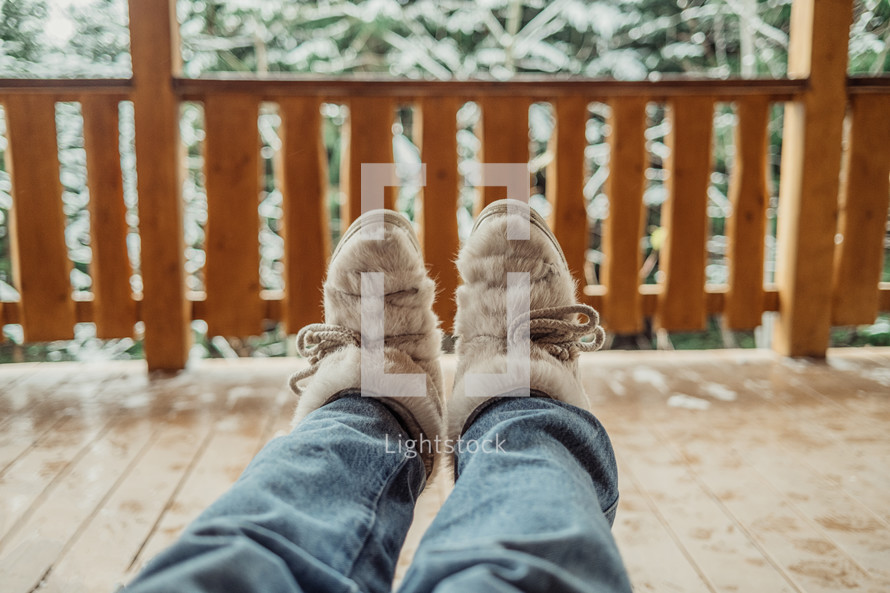 Woman legs in winter shoes - fur trendy boots on wooden balcony background. High quality photo