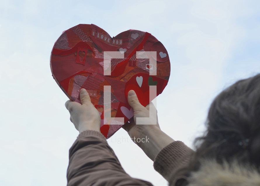woman holding up a paper heart heavenwards