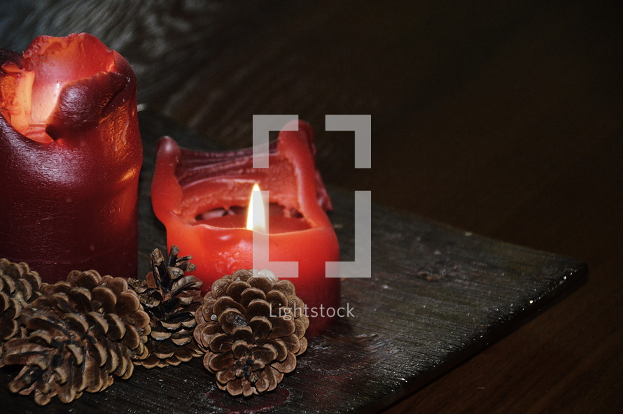 red candles with melting wax and pine cones 