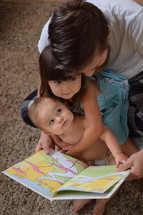 a father reading a book to his infant son and toddler daughter 