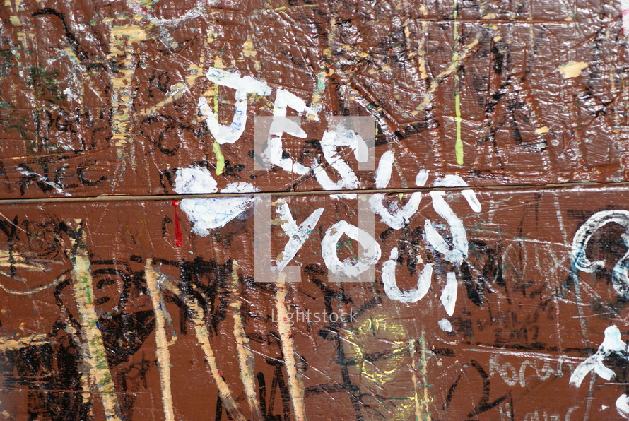 "Jesus loves you" written on a wall covered in graffiti.