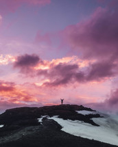 a man standing on a mountaintop under a purple sky with hands raised 