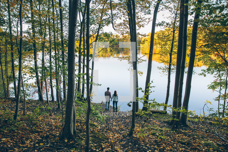 a couple standing by a lakeshore under a forest canopy 