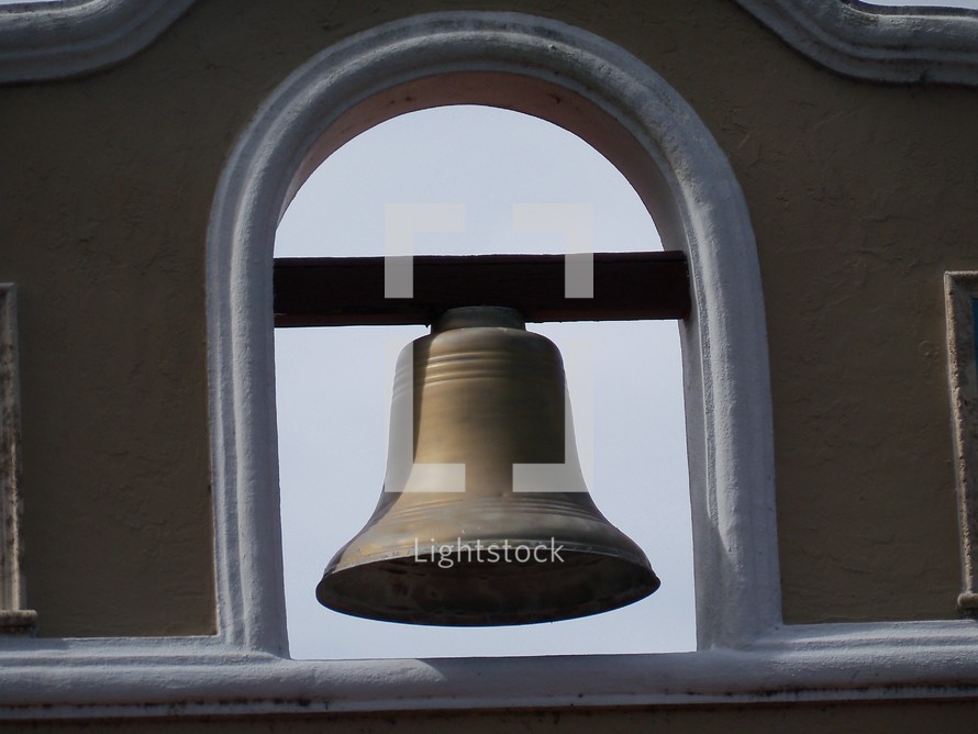 A large iron church bell adorning the tower of a local Spanish styled mission that rings to call people to worship. 