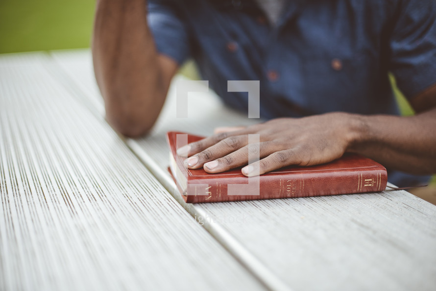 a man praying with his hand on a Bible 