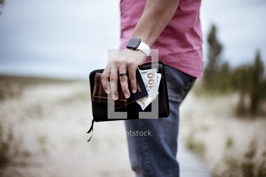 man holding a Bible, cash, and passport 