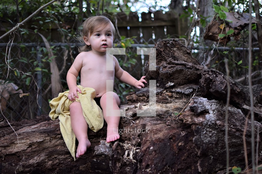 shirtless toddler boy sitting on a fallen tree 