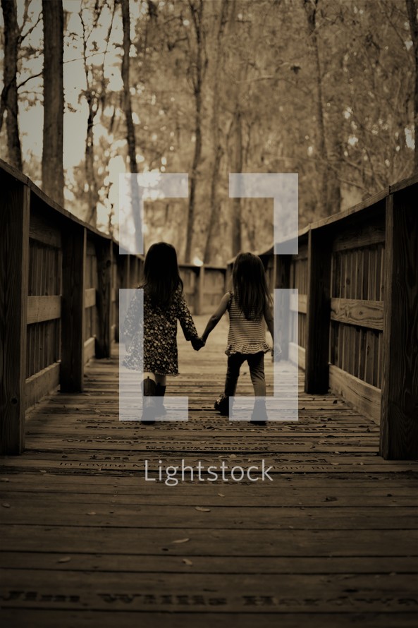 sisters walking on a boardwalk holding hands 