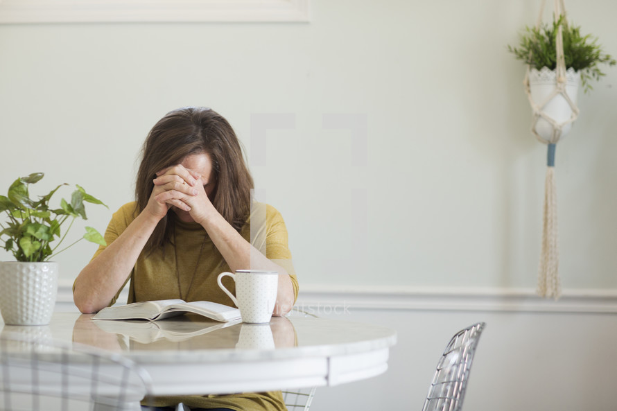 a woman praying over a Bible sitting at a kitchen table 