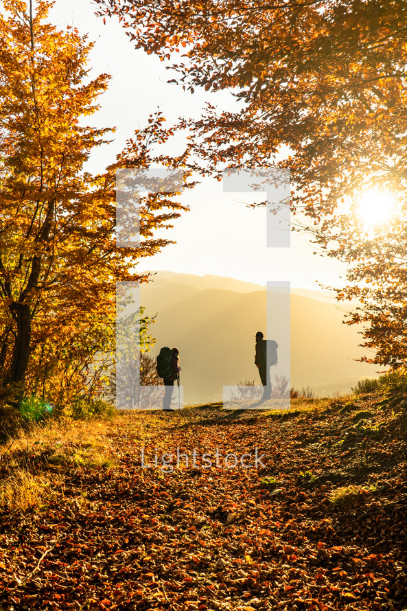 Silhouette of two hikers in autumn mountain forest