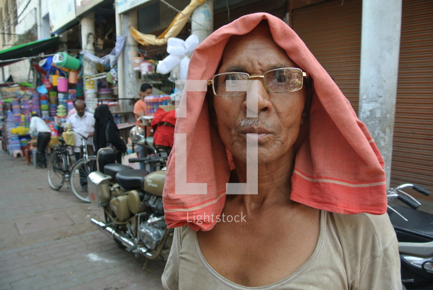 a man with a towel over his head standing in a street market 