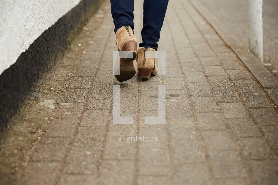 a woman walking on a brick sidewalk in heeled boots 