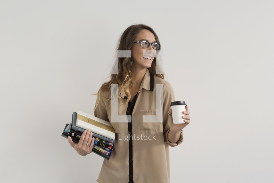 a college student holding a stack of books and a coffee cup 