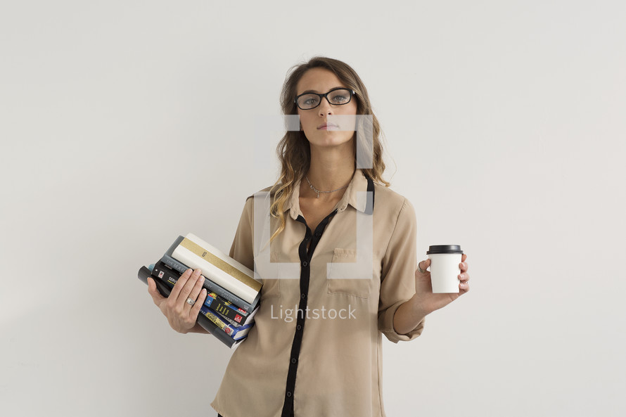 a woman holding a stack of books and a coffee cup 