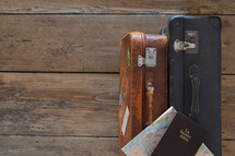 two old weathered suitcases with a map of Paris and a french bible on a rustic wooden floor