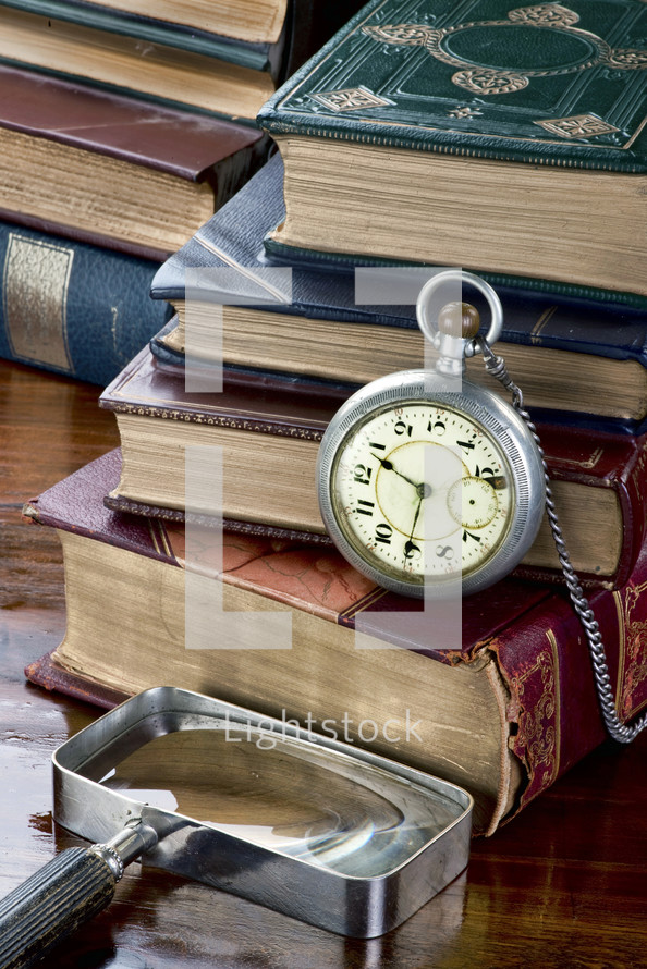 pocket watch, magnifying glass, and stacked books on a desk