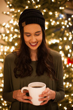 a woman holding hot cocoa in front of Christmas tree 