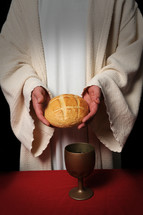 Priest hold a loaf of bread with a goblet of wine on the table