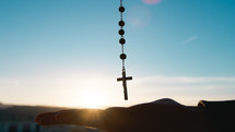 Silhouette of crucifix with sky background and hand on the bottom
