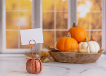 Orange and white pumpkins with a blank sign in front of autumn window