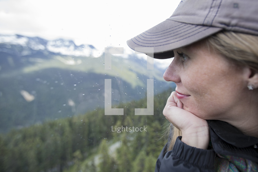 side profile of a woman in a ball cap looking out at mountains 