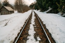 A railroad track by a log cabin in a snow covered landscape.