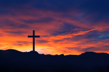 Silhouette of a cross on a hill under a red sky.