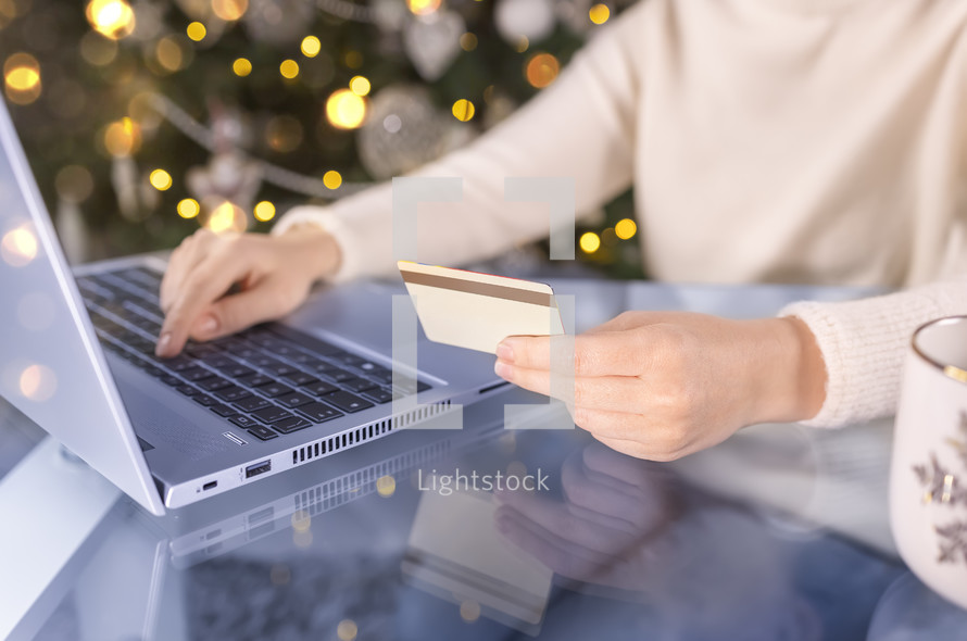 Woman using a credit card on a computer with a Christmas Tree in the background