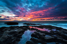 a purple and pink sky at sunset over tide pools 