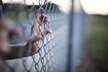 A hand gripping a chain link fence.