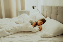 Calm little child sleeping well in comfortable bed. Boy with happy face and smile in light cozy bedroom. Healthy resting in morning, enjoying dreaming. High quality photo