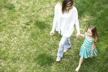a mother and daughter walking holding hands through grass