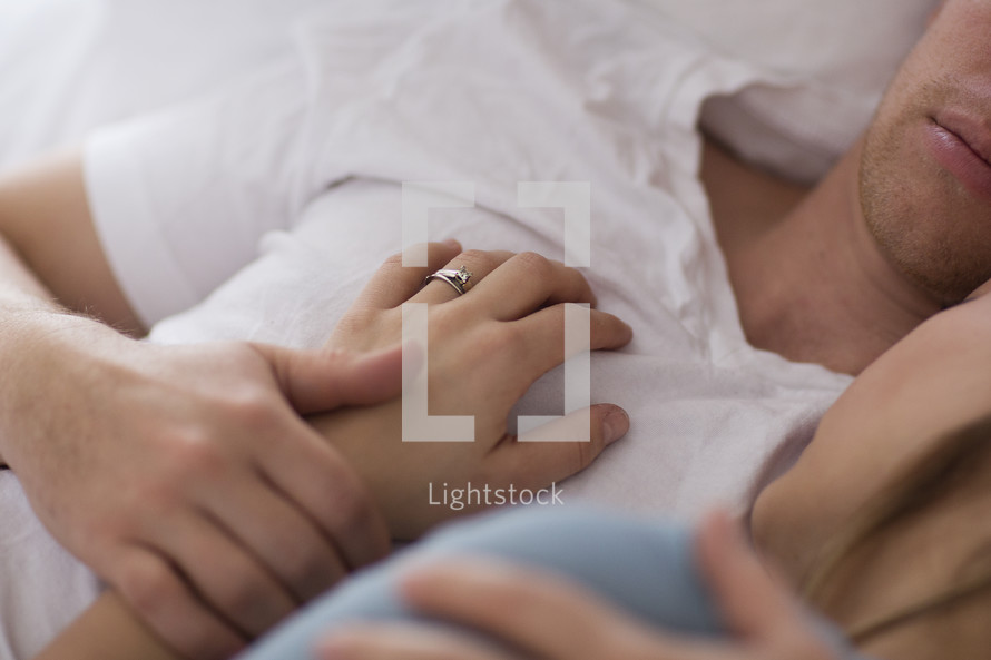 A woman's hand on her husband's chest as they lay in bed 